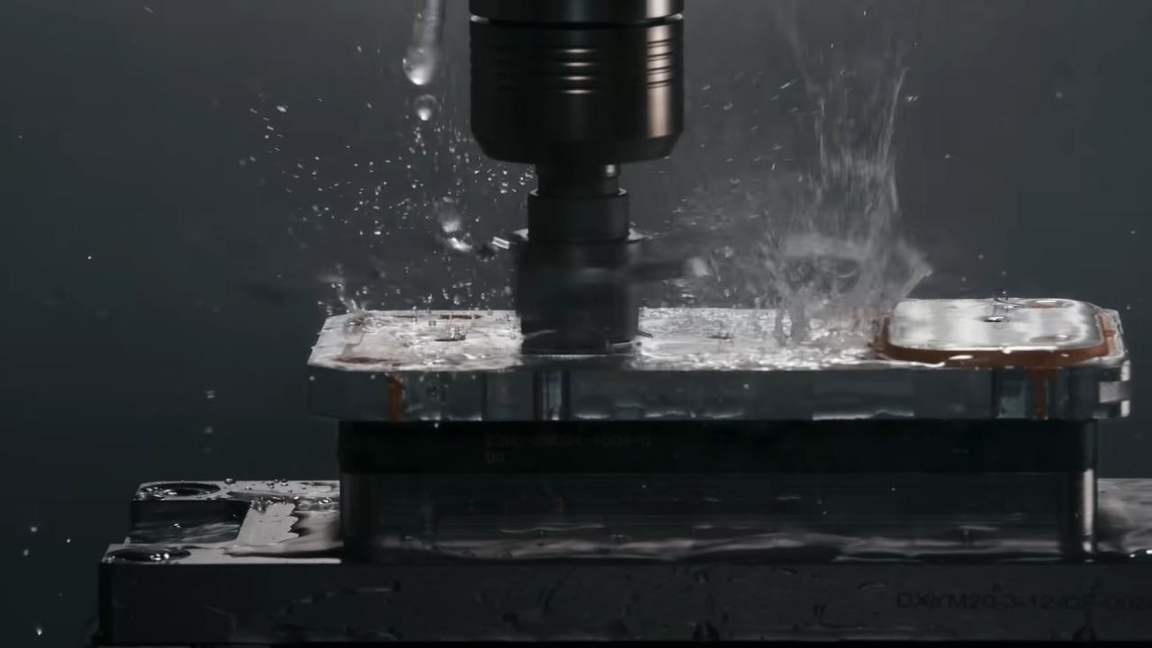 من موقع فون إسلام: صورة عن قرب لماكينة تفريز باستخدام الحاسب الآلي تقطع كتلة معدنية، مع تناثر سائل التبريد حول الأداة - الدقة في العمل تذكرنا بأجهزة التصنيع مثل آلة İ-فون إير.